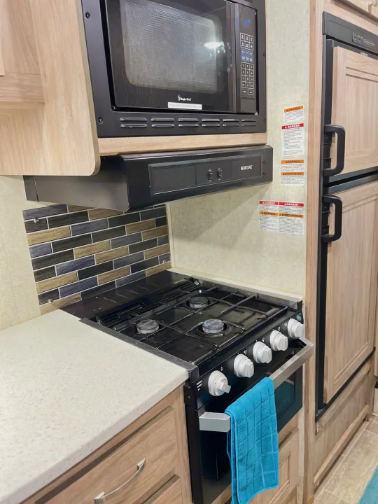 RV rental kitchen showing essential appliances: microwave, gas stovetop/oven, & refrigerator. Ready for your trip!. Forest River Sunseeker 2019