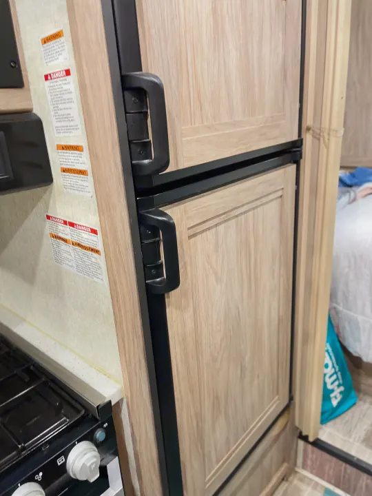 RV rental interior featuring a light wood-grain refrigerator, stove, and warning labels in a compact kitchen area.. Forest River Sunseeker 2019