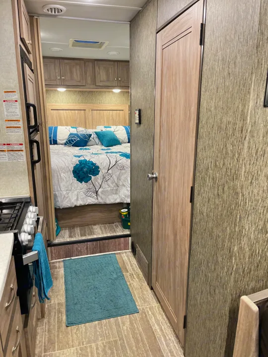 RV rental interior: kitchen galley to the left, a side door, and the bedroom with floral bedding visible ahead. Compact design.. Forest River Sunseeker 2019