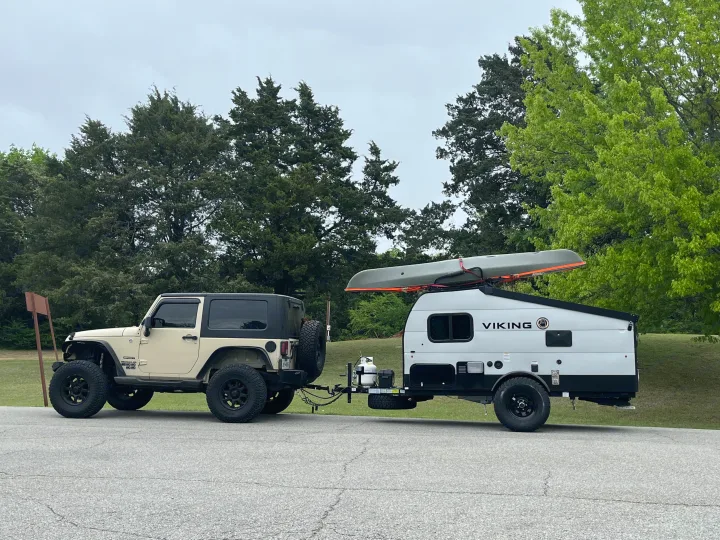 A beige Jeep tows a Viking rv rental camper with a canoe on top, ready for your next outdoor adventure.. Forest River Viking TD 2022