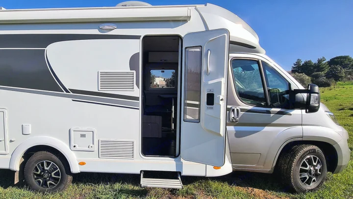 Side view of a white & gray RV rental with its side door open, revealing the interior & an extended step.. Carado T338 2022