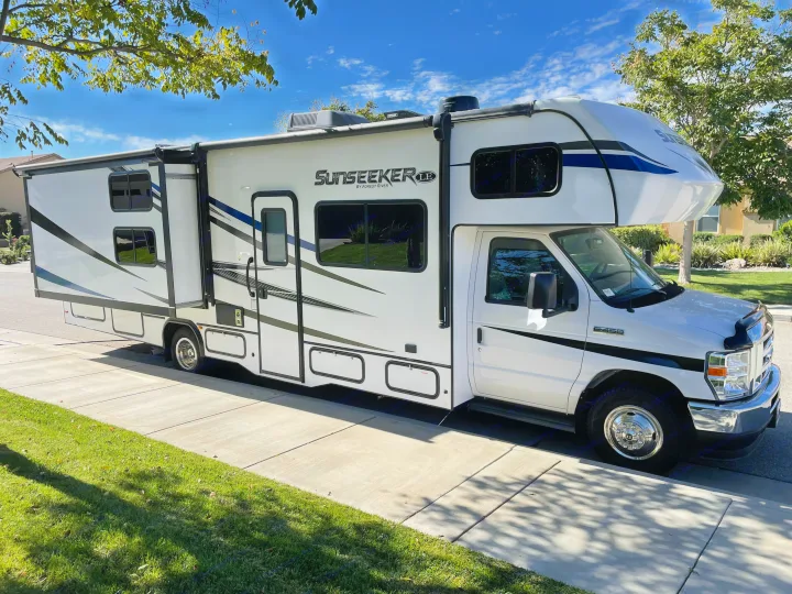 White Class C Sunseeker RV by Forest River, parked on street with slide-out. Ideal for your next RV rental adventure!. Forest River Sunseeker LE 2021