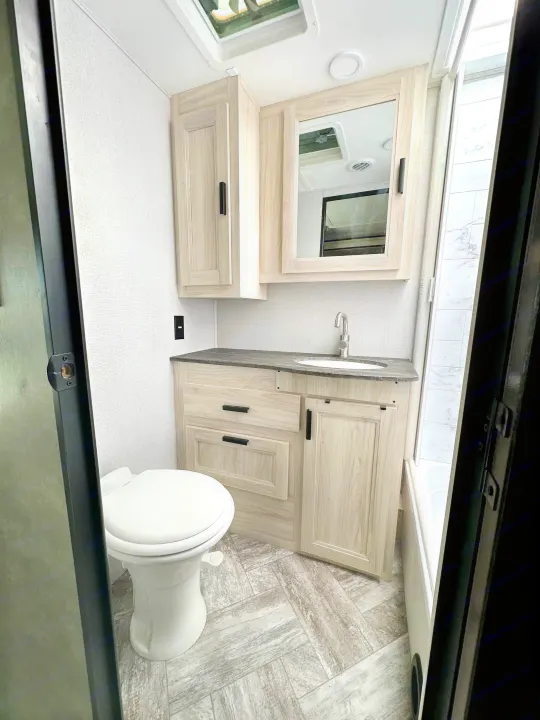 Modern RV rental bathroom interior, showing a white toilet, light wood vanity, sink, mirrored cabinet, and shower/tub.. Forest River Sunseeker LE 2021