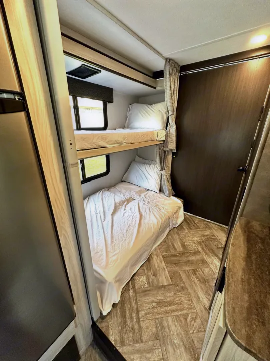 Inside an RV rental: Compact sleeping area with two bunk beds, bright windows, and tied-back curtains, providing a functional space.. Forest River Sunseeker LE 2021
