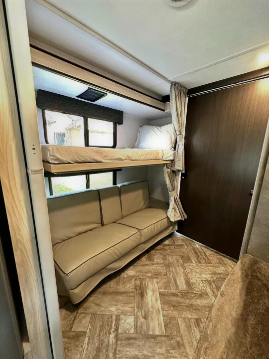 RV rental interior: Cozy bunk beds & sofa in a compact space, perfect for family travel adventures.. Forest River Sunseeker LE 2021