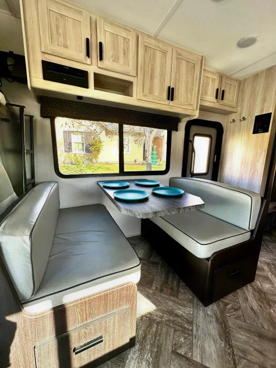 Cozy RV rental dinette featuring comfortable seating, overhead cabinets, a modern entertainment unit, and a scenic window view.. Forest River Sunseeker LE 2021