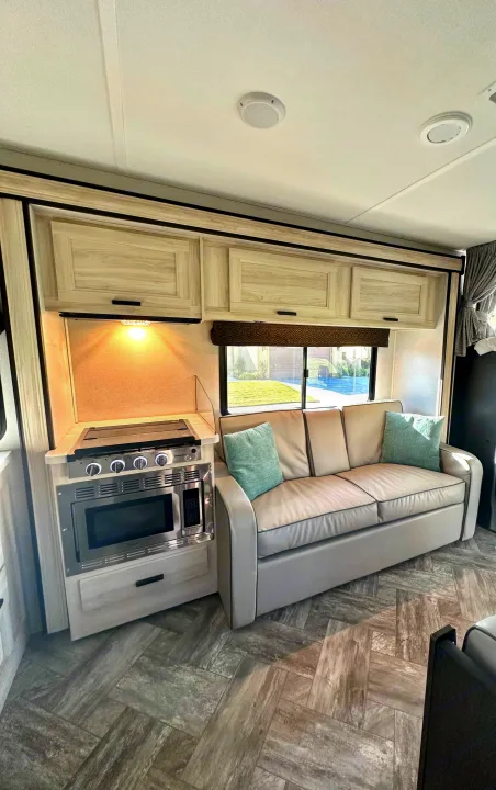 Modern rv rental interior: galley kitchen with cooktop & microwave, plush sofa, light wood-look cabinets, and stylish floor.. Forest River Sunseeker LE 2021