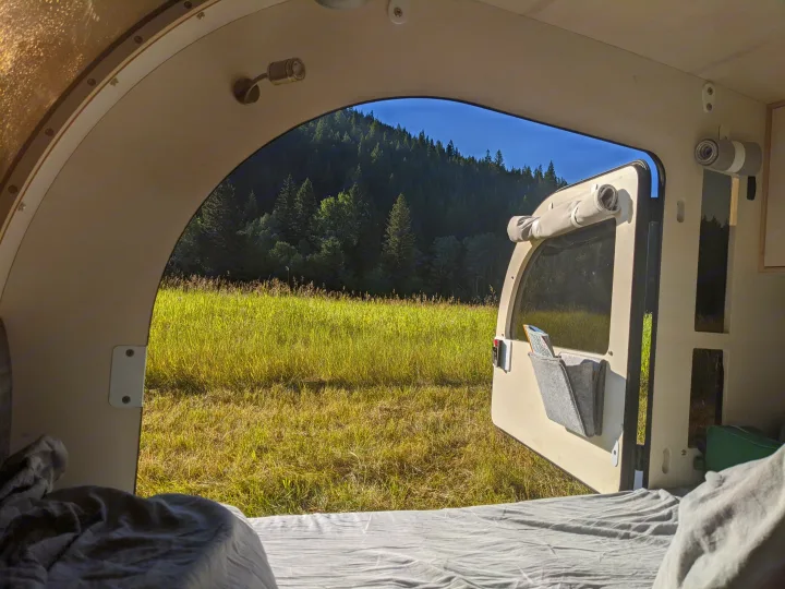 Enjoy a serene nature view from this cozy RV rental bed, overlooking a vibrant green field and dense forest.. droplet XL 2026