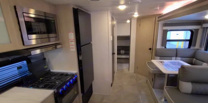 Inside a modern RV rental: well-equipped kitchen with microwave/stove, dining area, and sleeping space with bunk beds visible.. Forest River Other 2023