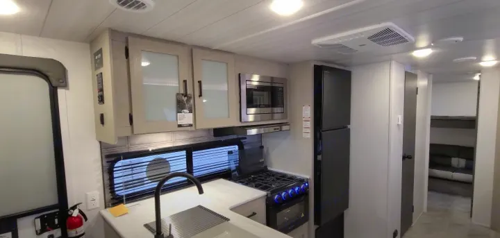 Inside an RV rental: a well-equipped kitchen featuring a stove, microwave, fridge, and sink. Bunk beds visible in the rear.. Forest River Other 2023