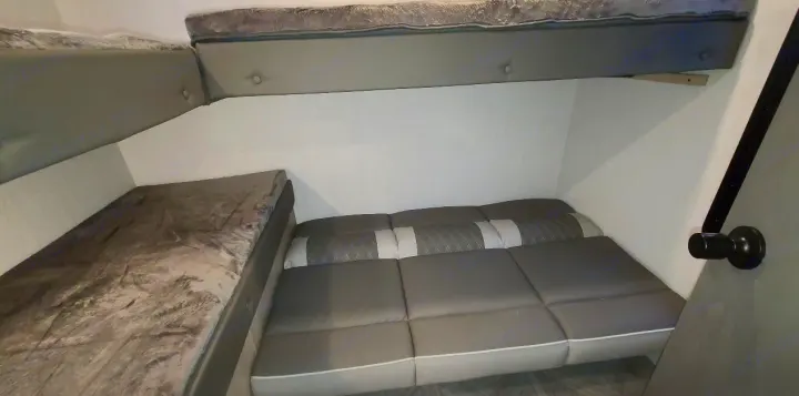 RV rental bunk beds: a top bed with a grey mattress, and a lower bed made of segmented grey cushions.. Forest River Other 2023