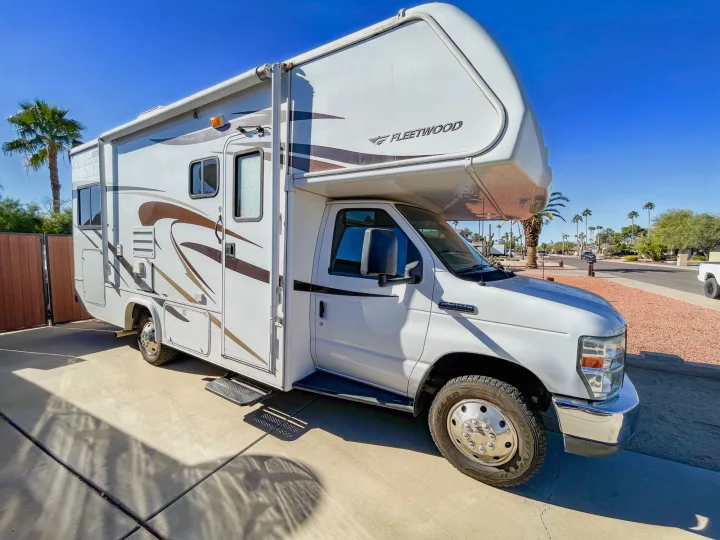 A white Fleetwood RV rental with brown accents, parked on a sunny driveway amidst palm trees. Perfect for your next adventure.. Fleetwood Jamboree 2012