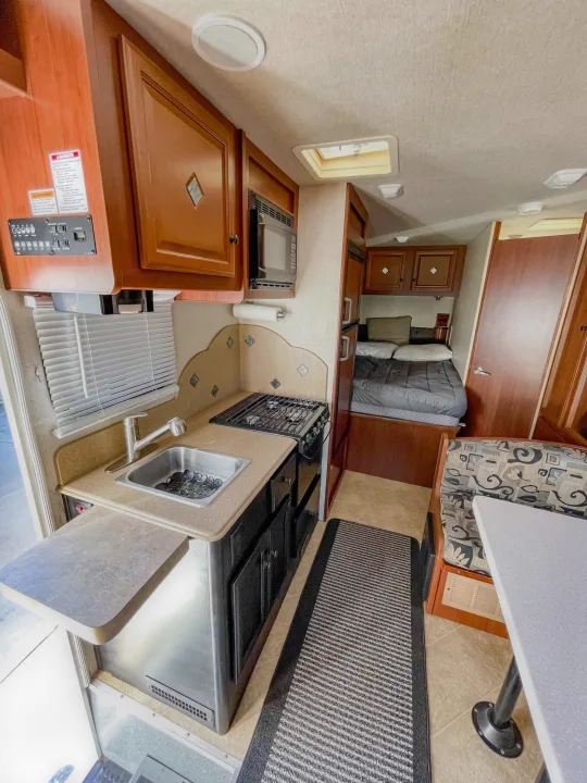 A compact RV rental interior showcasing a full kitchenette, a cozy sleeping area with a bed, and a dining nook.. Fleetwood Jamboree 2012