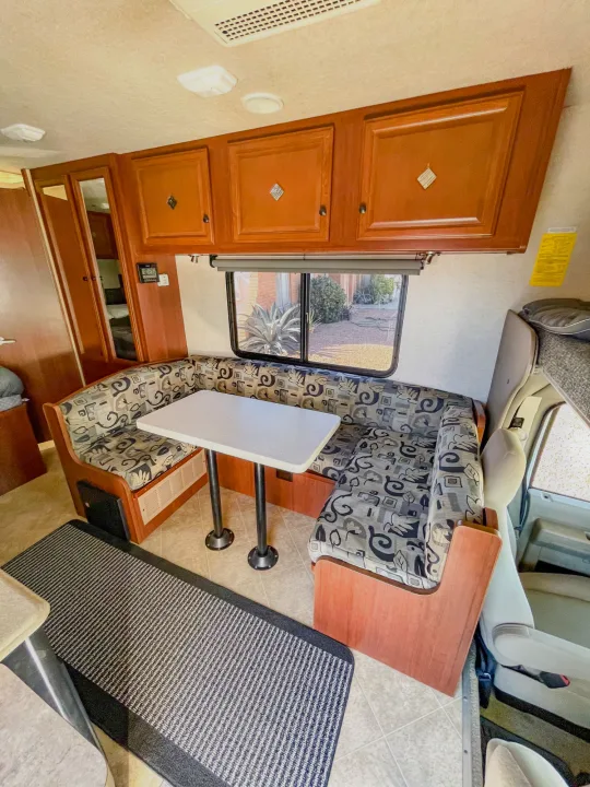 Spacious RV rental interior featuring a dinette with patterned cushions, wood cabinets, and a large window view.. Fleetwood Jamboree 2012