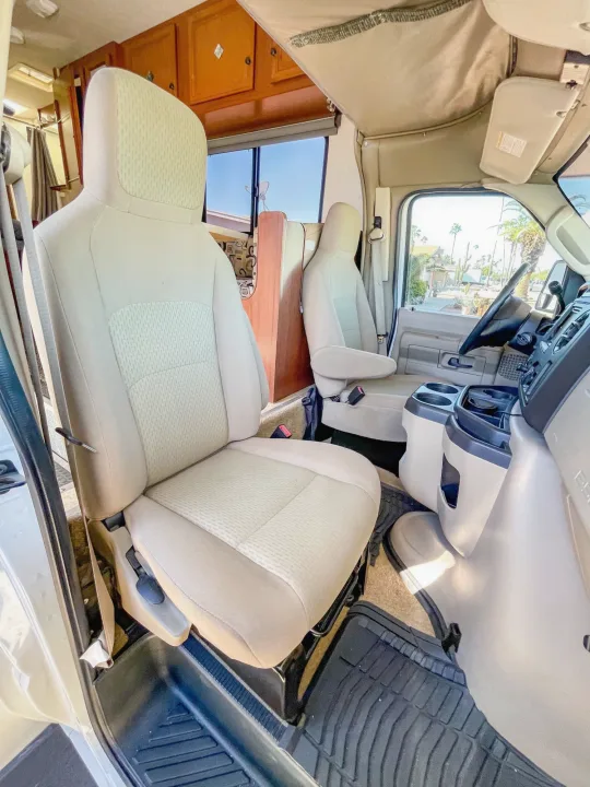 RV rental interior: Clean cockpit with beige driver's and passenger seats, dashboard, and rear living area visible.. Fleetwood Jamboree 2012