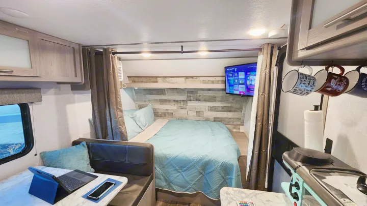 Cozy RV rental interior: A compact space with a bed, dinette, kitchen, and TV, perfect for travel and camping adventures.. Coleman Lantern 2023