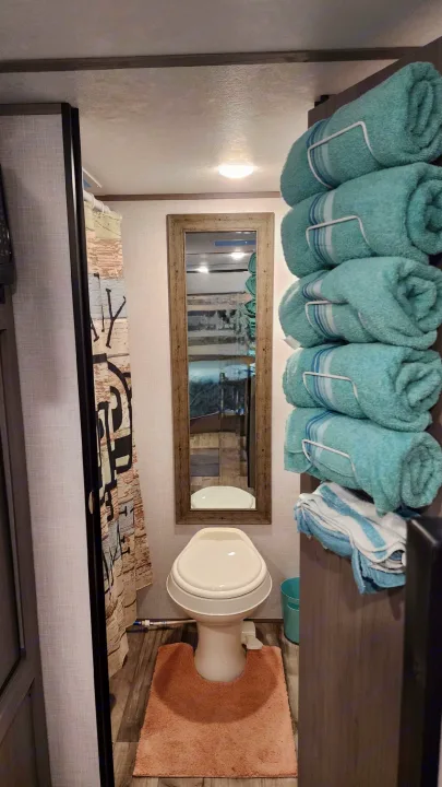RV rental interior: A clean, compact bathroom with a toilet, mirror, shower, and organized teal towels.. Coleman Lantern 2023