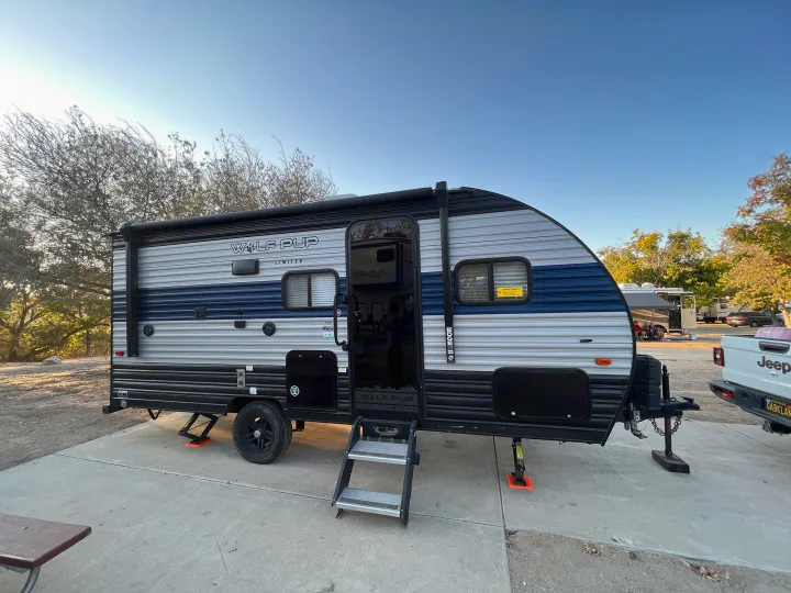 Modern Wolf Pup travel trailer, an ideal RV rental, fully set up with steps extended at a sunny, tree-lined campsite.. Forest River Cherokee Wolf Pup 2022