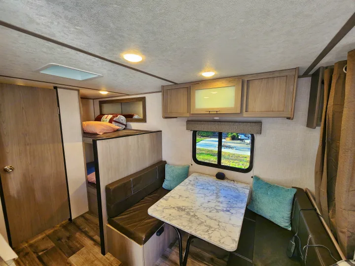 Bright RV rental interior featuring a cozy dinette with a faux marble table, bunk beds, and ample storage for travel.. Coleman Lantern 2023