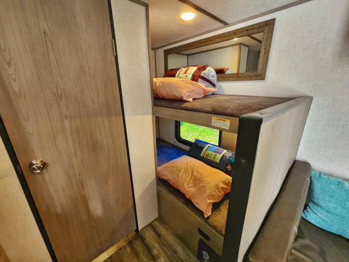Cozy RV rental interior featuring comfortable bunk beds with pillows, sleeping bags, and a window view. Ideal for family trips.. Coleman Lantern 2023