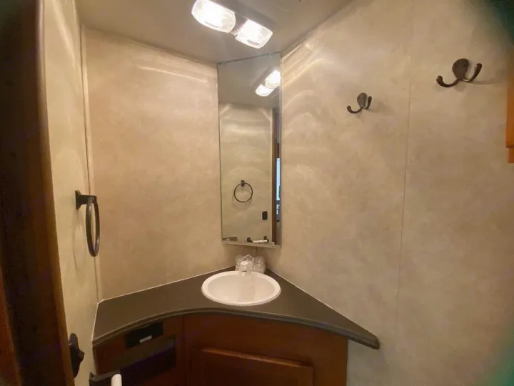 RV rental interior: Compact bathroom with a corner sink, mirror, overhead lights, and wall hooks for convenience.. Coachman Freelander 27QB 2011