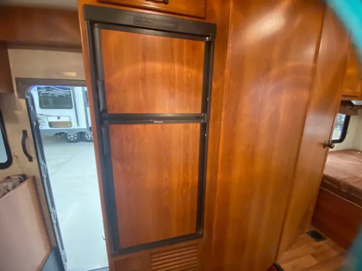 RV rental interior features a Dometic refrigerator with wood paneling, revealing an open doorway to another RV outside.. Coachman Freelander 27QB 2011