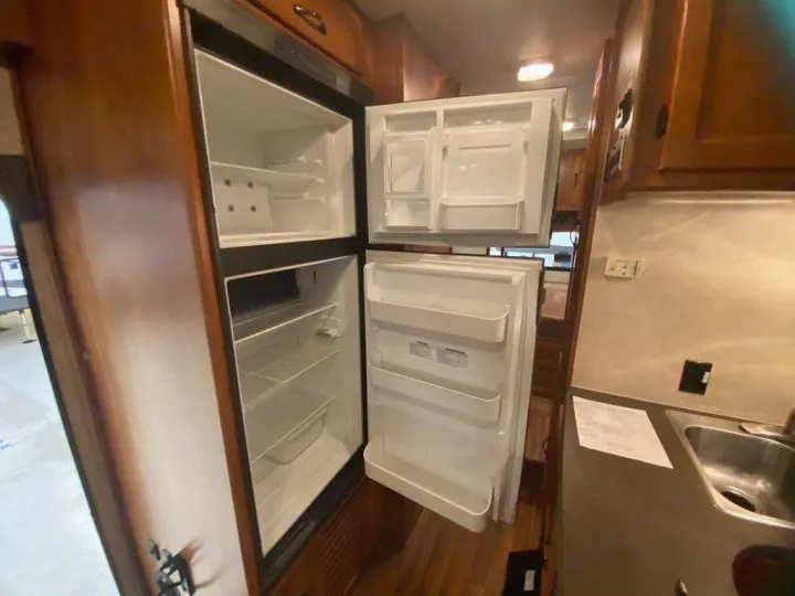 Interior view of an RV rental kitchen, featuring a clean, open two-door refrigerator and nearby sink.. Coachman Freelander 27QB 2011