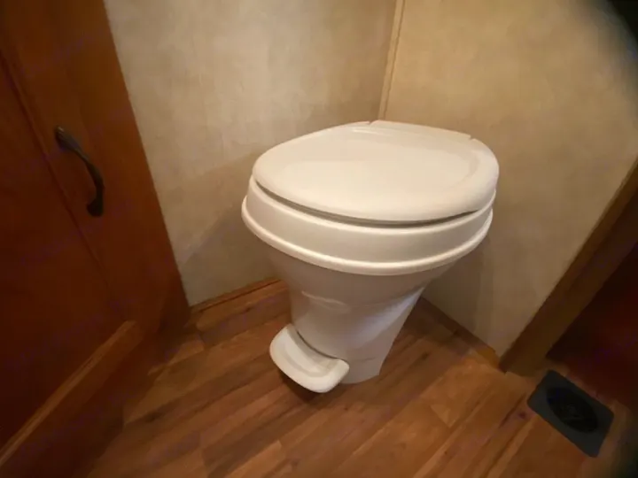 An RV rental's compact white toilet, featuring a foot flush mechanism, installed in a bathroom with wood-look flooring.. Coachman Freelander 27QB 2011