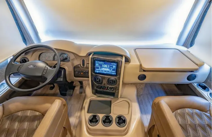 RV rental cockpit: Tan interior with Ford steering wheel, dashboard gauges, and infotainment screen displaying radio.. Thor Motor Coach Challenger 2019