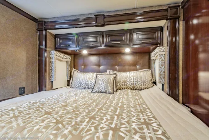 A comfortable RV rental bedroom interior with a large bed, tufted headboard, and stylish overhead storage, perfect for travel.. Thor Motor Coach Challenger 2019