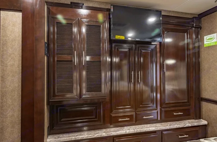 RV rental interior: dark wood cabinets, countertop, and TV. Ample storage for your adventures.. Thor Motor Coach Challenger 2019