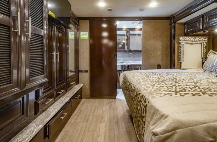 Spacious RV rental bedroom featuring rich wood cabinetry, a comfortable bed, and an en-suite bathroom behind a sliding door.. Thor Motor Coach Challenger 2019