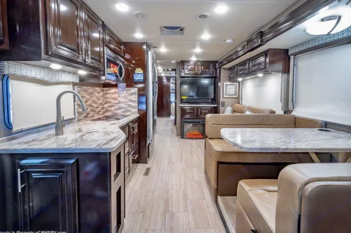 Spacious, modern RV rental interior featuring a full kitchen, dining banquette, and cozy living area with TV and fireplace.. Thor Motor Coach Challenger 2019