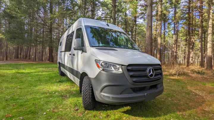 White Mercedes Sprinter camper van, an ideal RV rental for forest camping and nature adventures. Parked on grass.. Mercedes-Benz Sprinter 2020