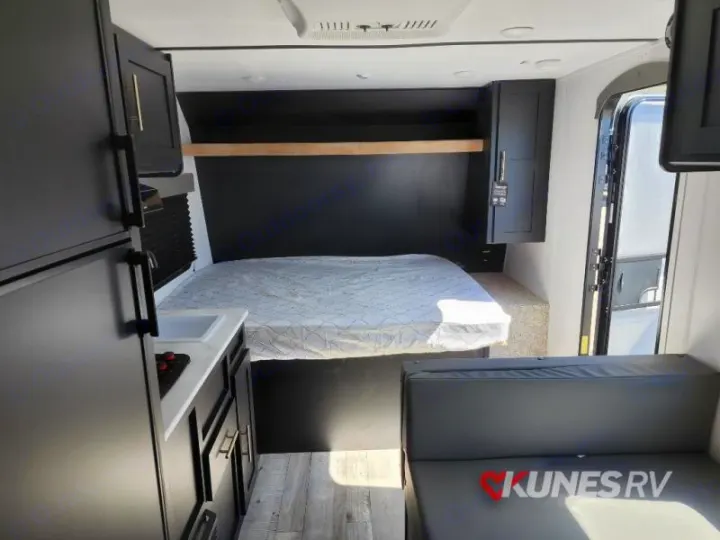 View inside a modern RV rental: a bed with black headboard, compact kitchen, and gray sofa, showing efficient use of space.. Keystone Springdale 2022