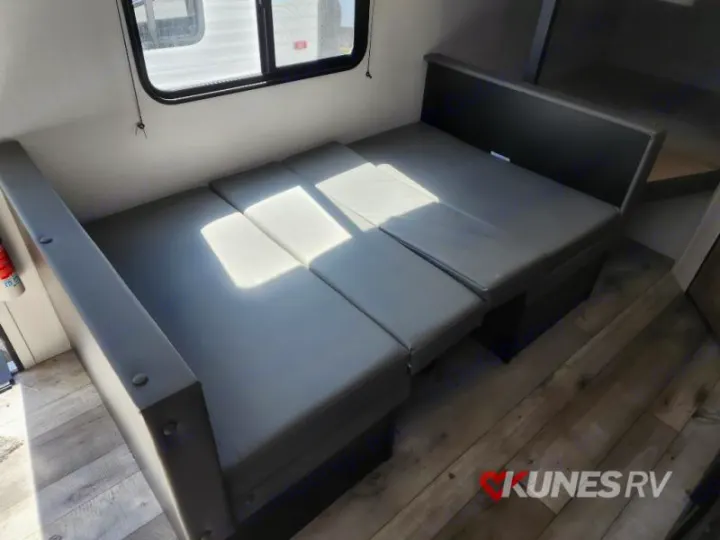 Inside an RV rental: Grey cushions form a dinette that converts to a bed, brightened by sunlight.. Keystone Springdale 2022