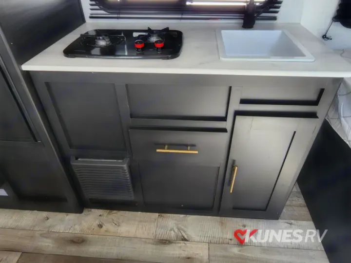 An RV rental kitchenette with a two-burner stove, sink, and stylish dark cabinets, ideal for your travels.. Keystone Springdale 2022