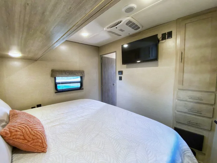 Spacious RV rental bedroom featuring a comfortable bed, window, wall-mounted TV, and ample built-in storage.. Coachmen Catalina 2022