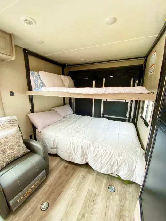 Comfortable RV rental interior with light walls, wood-look floor, bunk beds, and a gray recliner.. Coachmen Catalina 2022