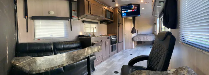 View of a modern RV rental interior featuring a living area with black sofa and table, full kitchen, wall-mounted TV, and a rear bedroom.. Genesis Supreme Rv Genesis Supreme 2022