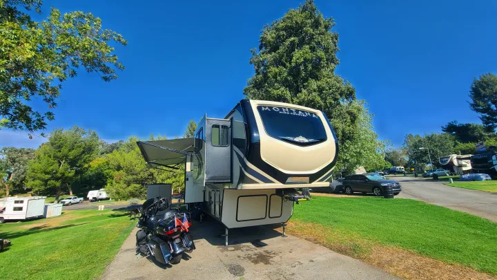 Modern Montana High Country fifth-wheel RV and motorcycle parked at a sunny campground.. Keystone RV Montana High Country Toy Hauler 2019