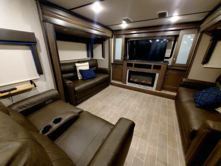 Cozy RV rental living space: brown leather recliners, TV, electric fireplace, and wood-look flooring.. Keystone RV Montana High Country Toy Hauler 2019