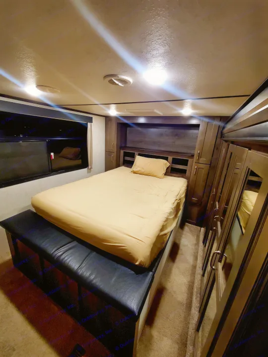 Comfortable RV rental bedroom with warm lighting, featuring a spacious bed, built-in storage, and mirrored wardrobe.. Keystone RV Montana High Country Toy Hauler 2019