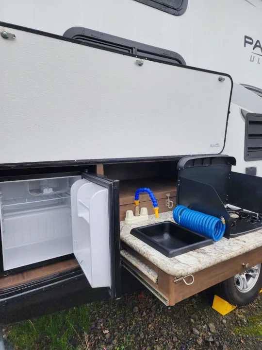 Outdoor kitchen on an RV rental: mini-fridge, sink, stove, and flexible faucet. Ideal for easy camping convenience.. Keystone RV Passport Grand Touring 2018