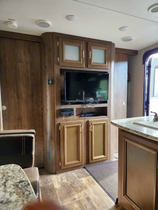 RV rental interior: cozy living space with media center, TV, kitchen counter, and wood cabinetry.. Keystone RV Passport Grand Touring 2018