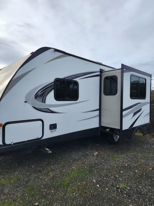 Side view of a white travel trailer with gray graphics & extended slide-out. Perfect for your next RV rental.. Keystone RV Passport Grand Touring 2018