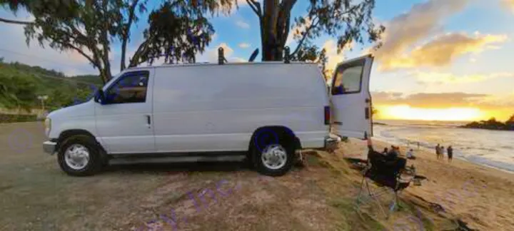 White RV rental van enjoying a stunning beach sunset. Open doors, chairs, and ocean views for a perfect getaway.. Ford E250 2009
