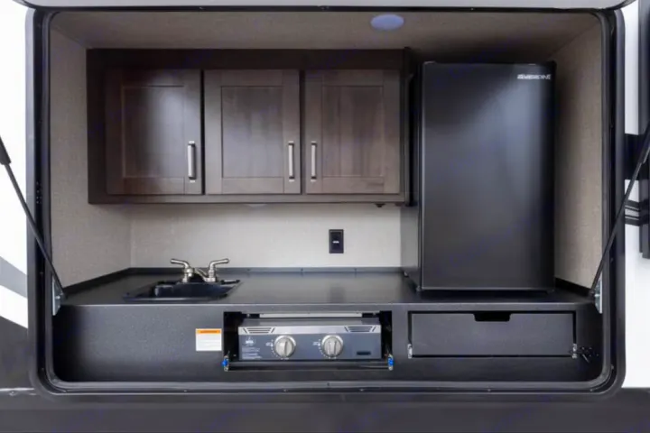 Enjoy an RV rental with this fully equipped outdoor kitchen. Features a sink, fridge, slide-out grill, and overhead cabinets for camp cooking.. Grand Design Reflection 2022
