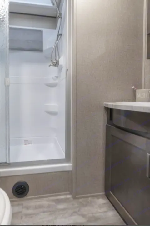 Inside an RV rental bathroom, featuring a bright white shower with glass door and a stylish dark wood vanity. Compact and functional.. Grand Design Reflection 2022