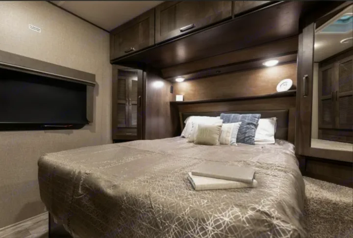 Comfortable RV rental bedroom featuring a large bed, wall-mounted TV, and ample storage cabinets.. Grand Design Reflection 2022